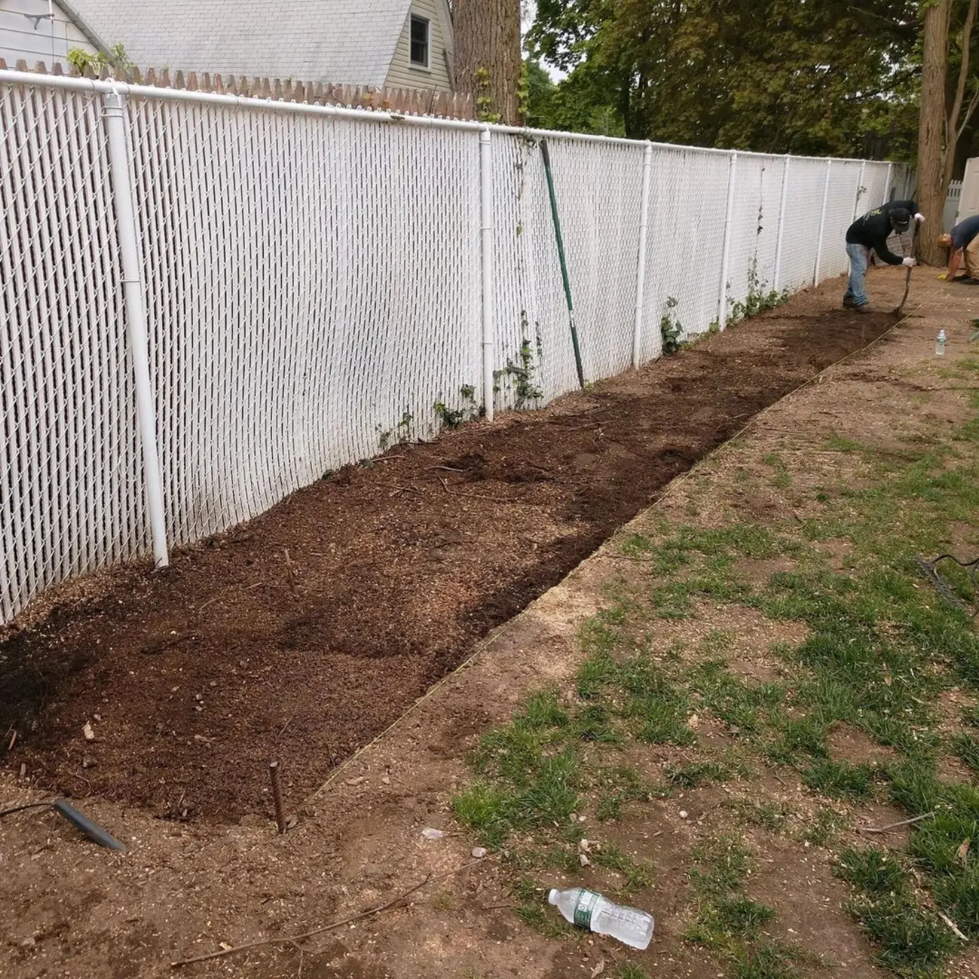 Crew digging a new bed line along a chain link fence