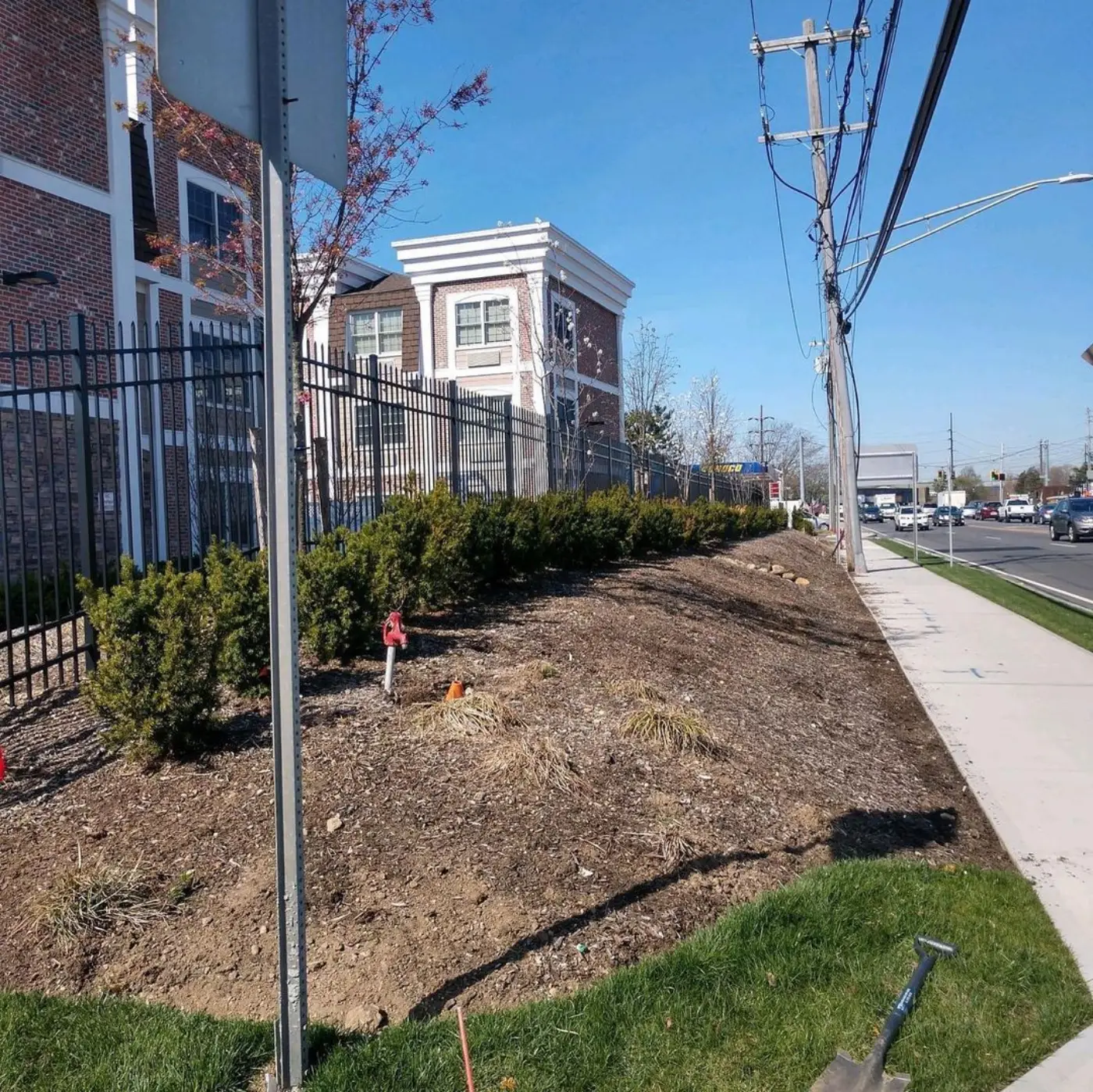 Commercial frontage with bare, weedy beds along an iron fence