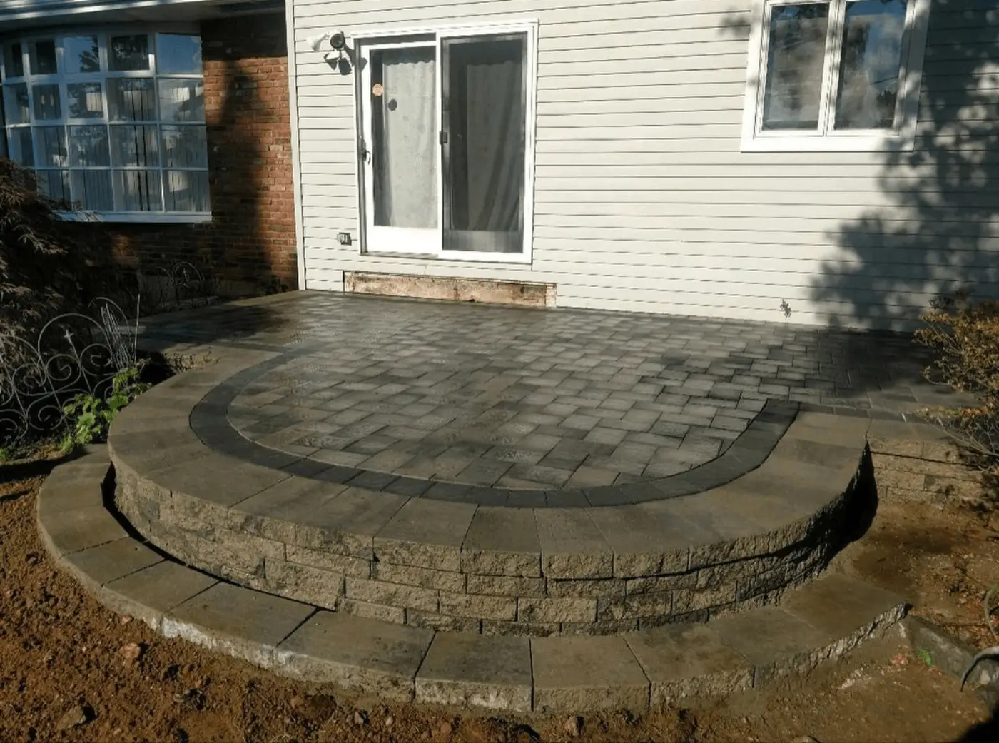 Curved paver patio with a stacked stone step leading to a back door