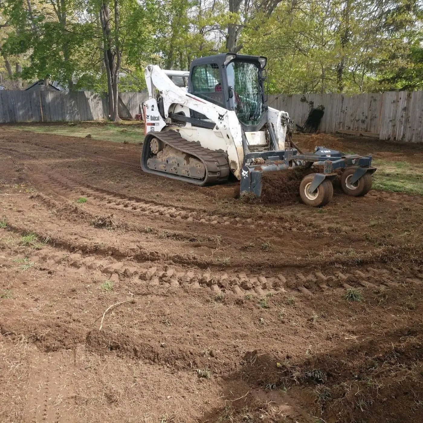 Skid steer with a harley rake grading a bare backyard