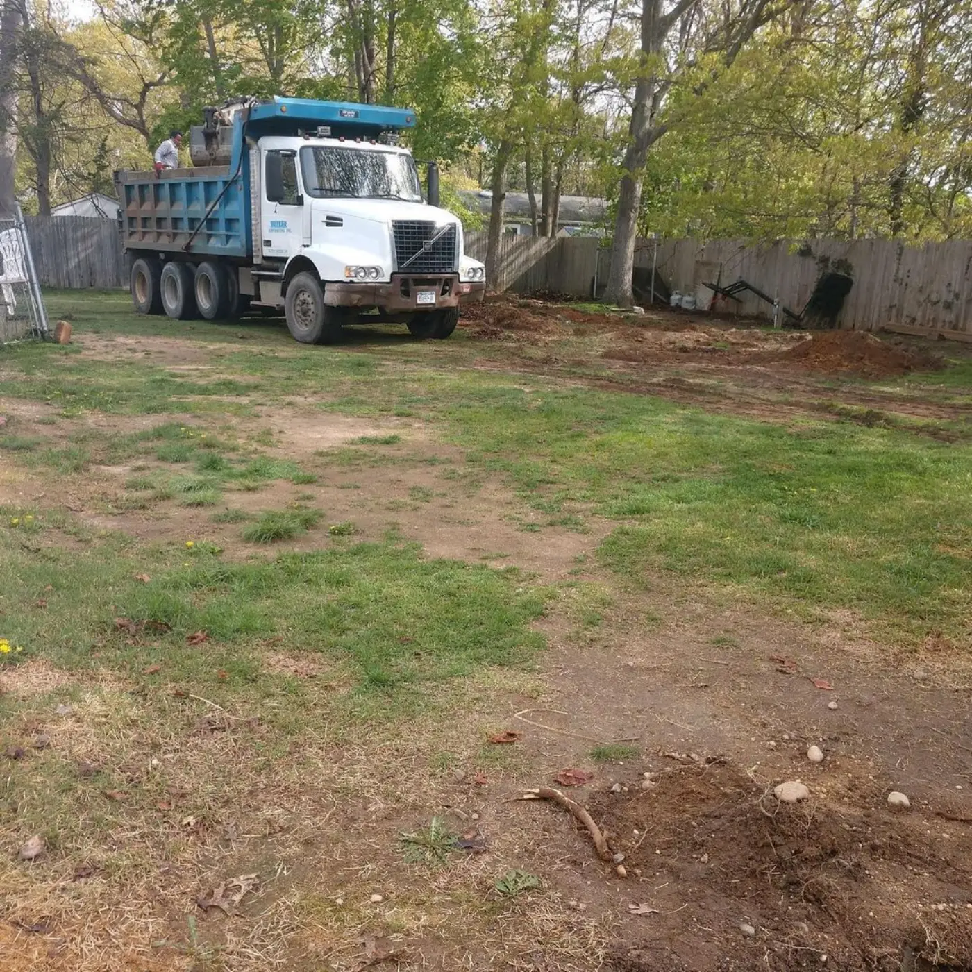 Dump truck delivering topsoil into a cleared backyard